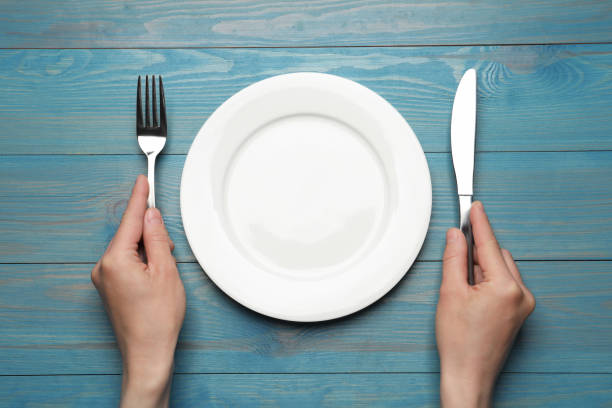 Woman with empty plate and cutlery at blue wooden table, top view